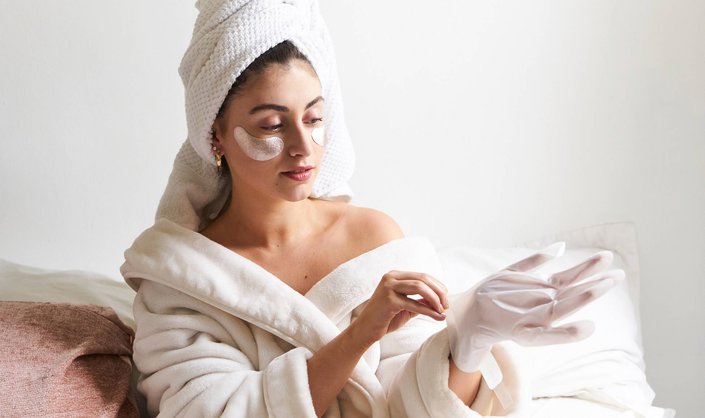 person applying a glove hand mask onto their hand, while wearing a bathrobe