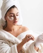 person applying a glove hand mask onto their hand, while wearing a bathrobe