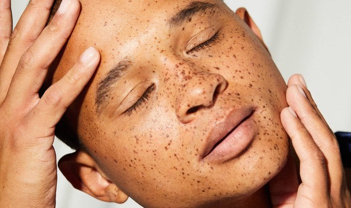 person touching face with closed eyes facing toward the camera