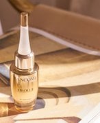 lancome l'absolu serum photographed on a gold-beige magazine background
