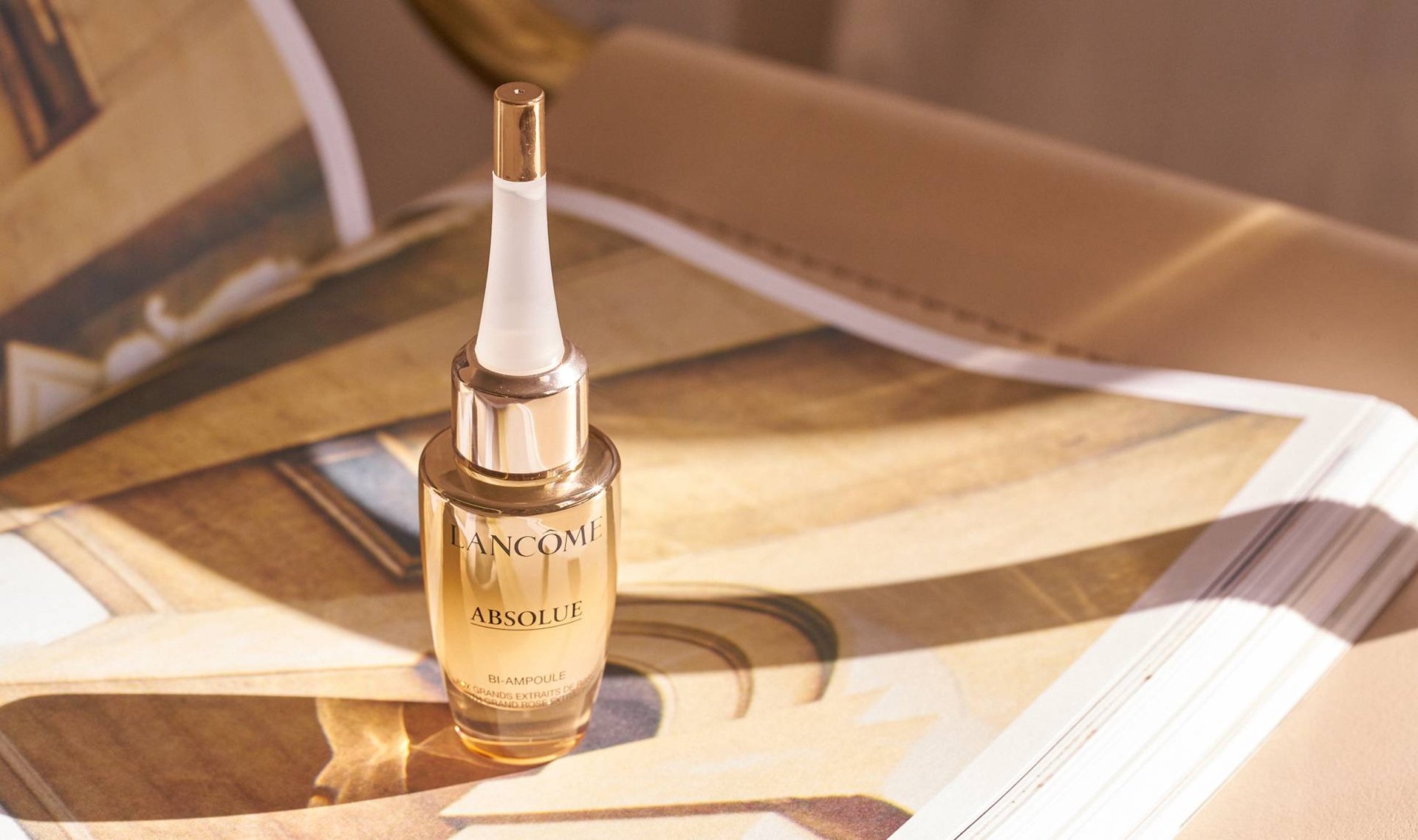 lancome l'absolu serum photographed on a gold-beige magazine background