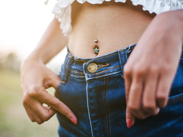 Close-up of a stomach with a belly button piercing with star-shaped jewelry. The person is wearing a white shirt and blue jeans.
