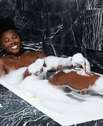 Person sitting in a bubble bath and smiling with one leg out of the water, touching their leg