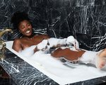 Person sitting in a bubble bath and smiling with one leg out of the water, touching their leg 