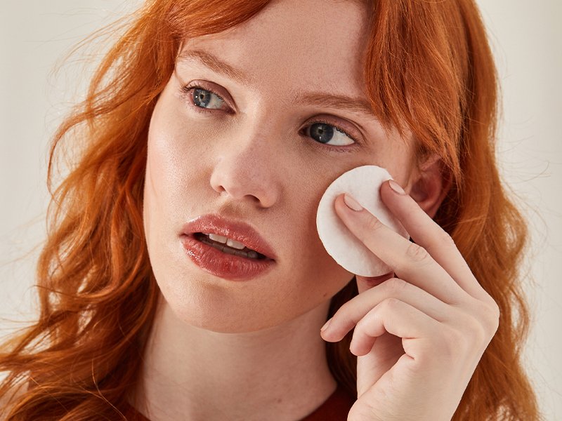 Image of woman with red hair holding a cotton round against her cheek