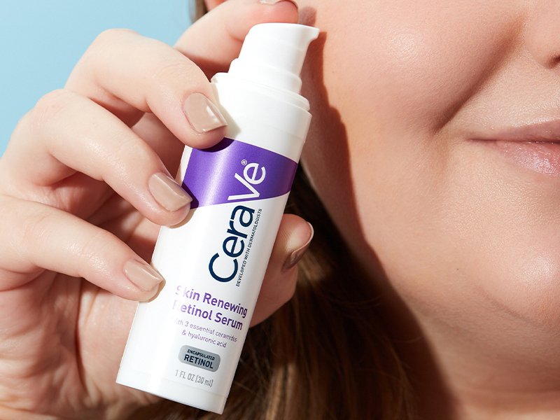 A person holding the CeraVe Skin Renewing Retinol Serum bottle close to their face.