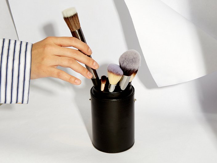Image of a model taking a makeup brush out of a black cup full of other makeup brushes