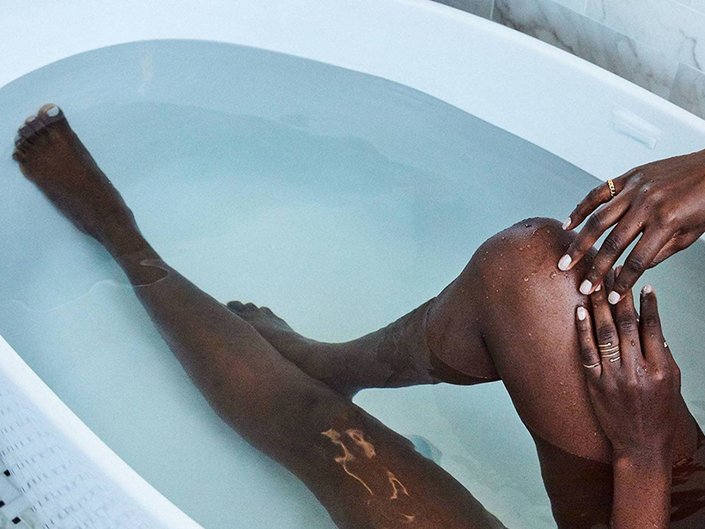 A person's legs in a filled bathtub, one knee bended up and hands resting on the knee.