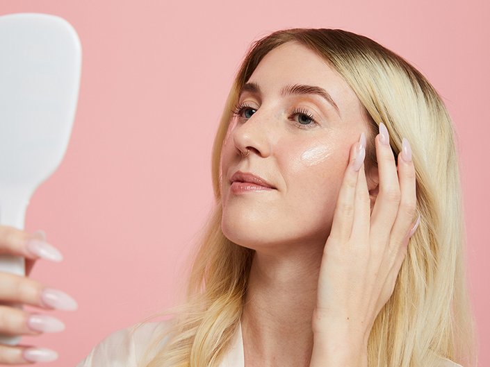 person touching their face and looking in a hand mirror