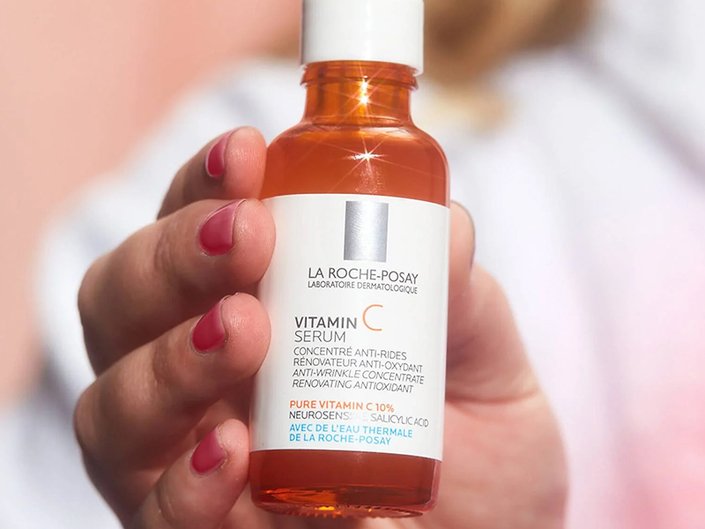 Close-up of a person’s hand with pink painted nails holding up the La Roche-Posay Vitamin C Serum