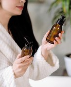Picture of a model wearing a white bathrobe and holding two empty brown glass bottles