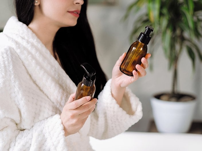 Picture of a model wearing a white bathrobe and holding two empty brown glass bottles