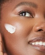 Picture of a person applying a white cream on their cheek.