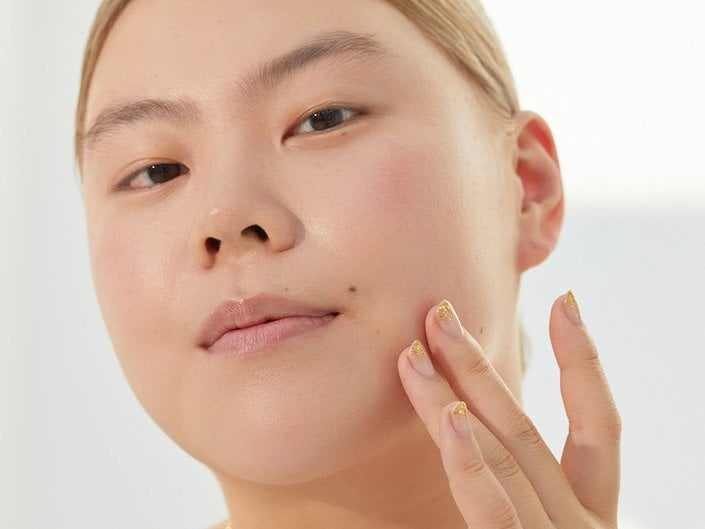 Close-up picture of a model looking at the camera and touching the side of their chin