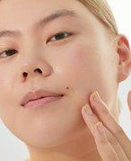 Close-up picture of a model looking at the camera and touching the side of their chin