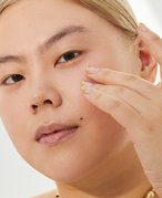 Close-up picture of a model looking at the camera and touching their cheek