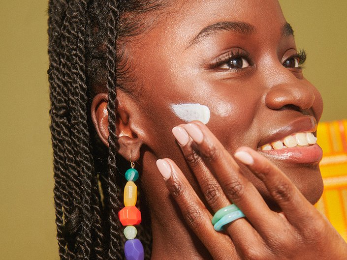 Black model smiling and applying sunscreen to her cheek
