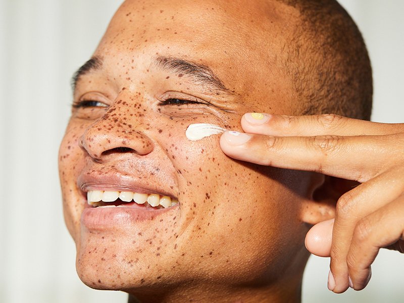 Photo fo a person smiling and applying balm underneath their eye