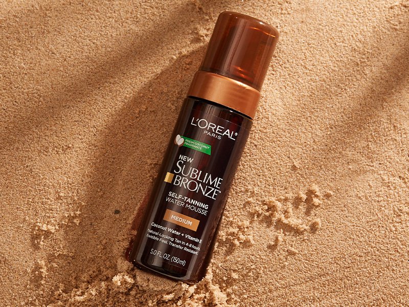 An image of the L'Oréal Paris Skincare Sublime Bronze Self-Tanning Water Mousse on top of sand