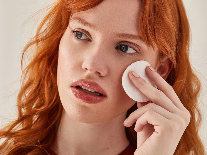 Close-up picture of a red-haired model holding a cotton toner pad to their cheek