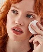 Close-up picture of a red-haired model holding a cotton toner pad to their cheek