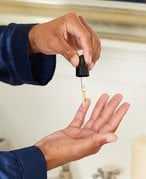 Picture of one hand with a dropper squeezing product onto another hand directly below
