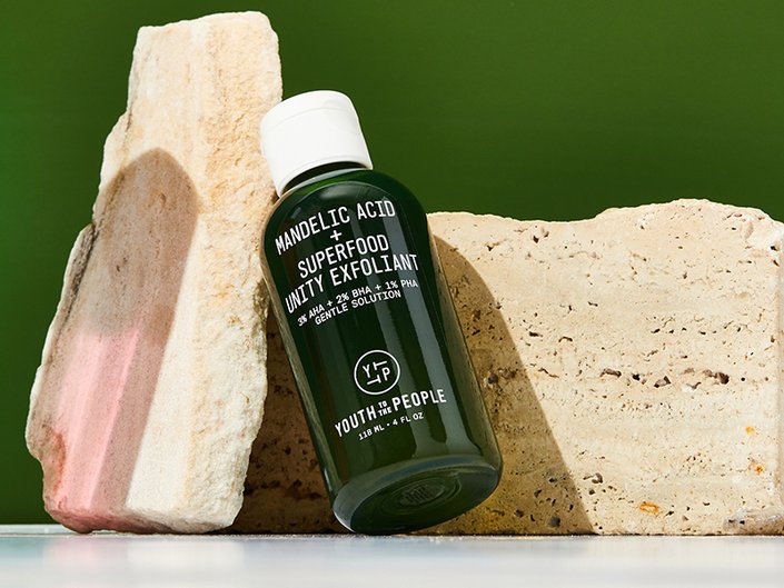 Picture of the Youth To The People Mandelic Superfood Unity Exfoliant leaning against two rocks on a dark green background
