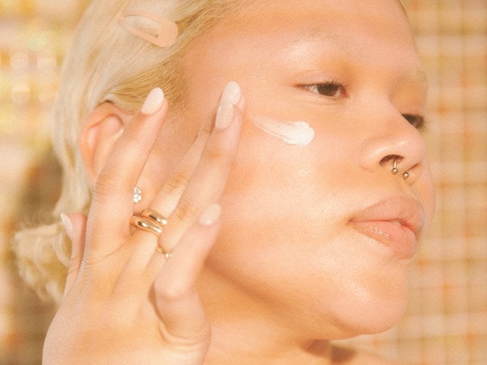 Person with bleached blonde hair swatching face cream into their cheek