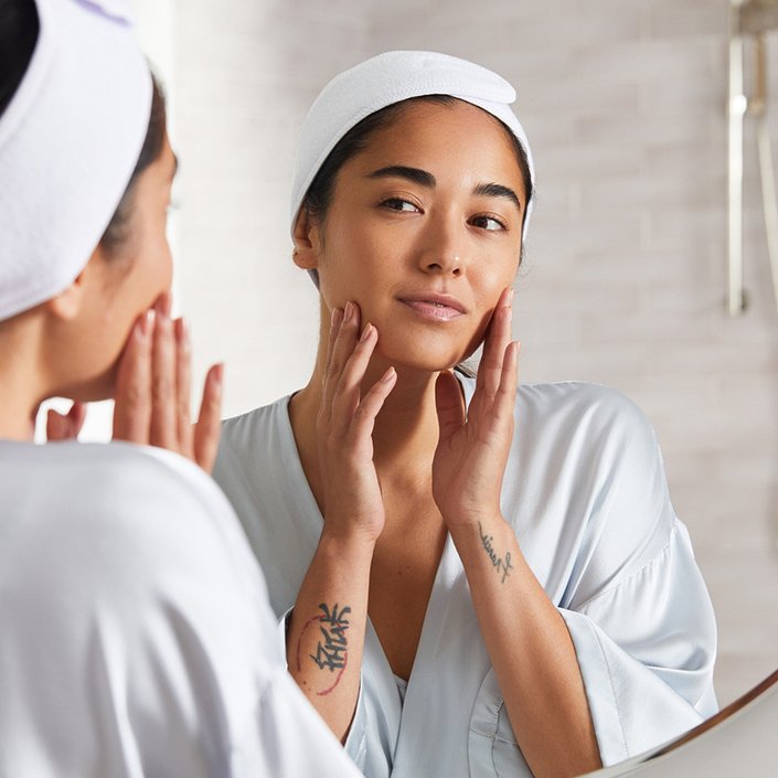 Picture of a model looking in the mirror and touching the sides of their face