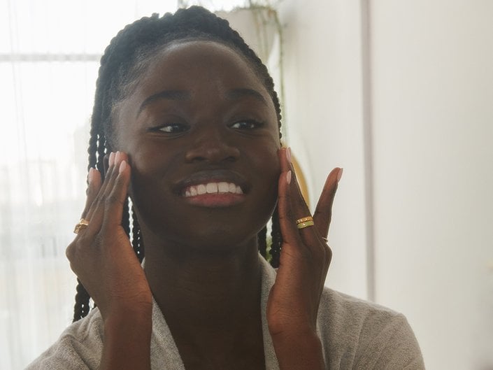 Person wearing a gray bathrobe smiling and touching their cheeks with their fingertips