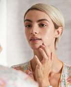 Picture of a model looking at their reflection in the mirror and applying spot treatment