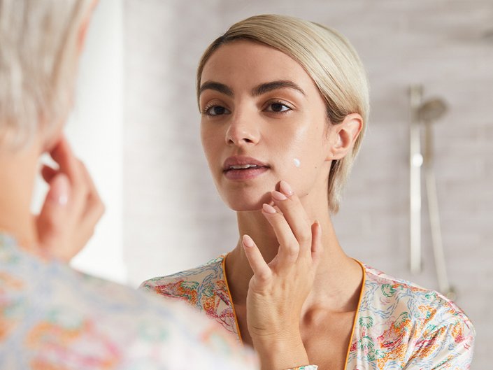 Picture of a model looking at their reflection in the mirror and applying spot treatment
