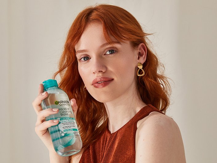 Picture of a red-haired model looking at the camera while holding a Garnier micellar water