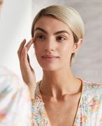 Person with a blonde pixie cut looking in the mirror and touching their fingers to their eyebrow