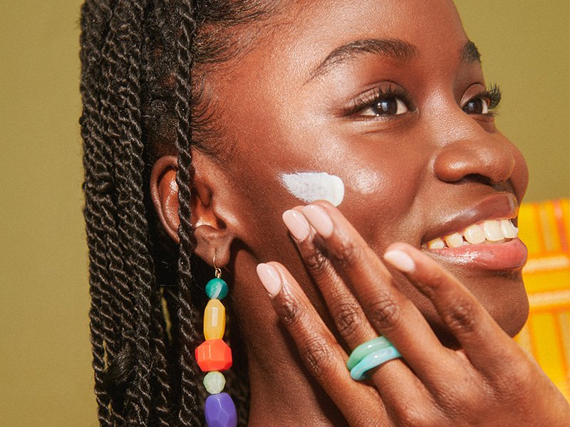 Black model smiling and applying sunscreen to their cheek