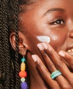 Black model smiling and applying sunscreen to their cheek