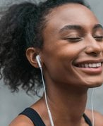 Person with dark hair pulled back in a ponytail smiling with their eyes closed and wearing earphones