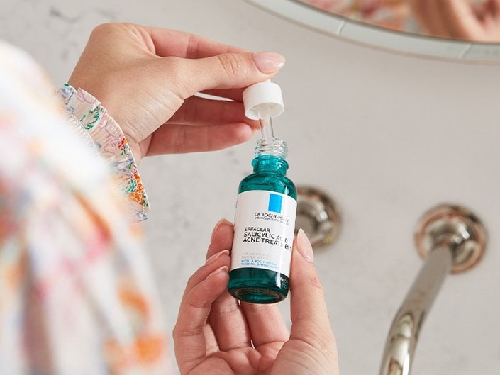 person holding acne serum bottle with dropper