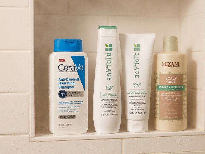 An image featuring  Cerave Anti-Dandruff Hydrating Shampoo, Biolage Scalp Sync Clarifying Shampoo + Universal Conditioner, and Mizani Scalp Care Shampoo displayed on shower shelving/a shower rack.