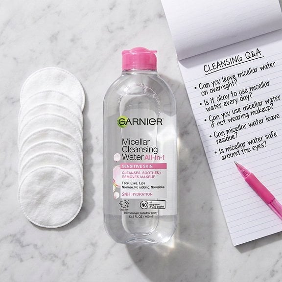 A flat lay of micellar water, a stack of cotton pads, and a “Q&A” or FAQ notepad, symbolizing answers to common cleansing questions.