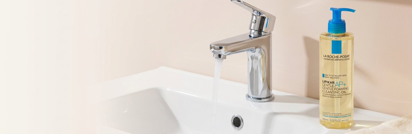 A bathroom sink with the water running and a bottle of La Roche-Posay Lipikar AP+ Gentle Foaming Cleansing Oil next to it.